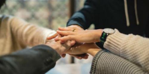 Four people in circle with their hands stacked in the middle